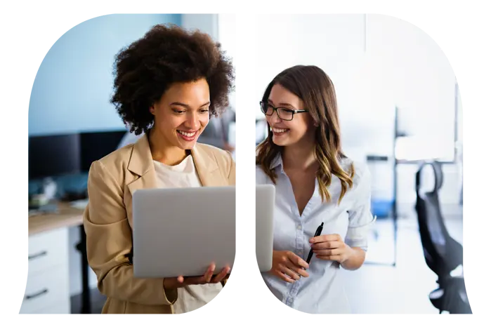 A professional working woman who is holding a pen is looking at another professional working woman who is looking at her laptop.