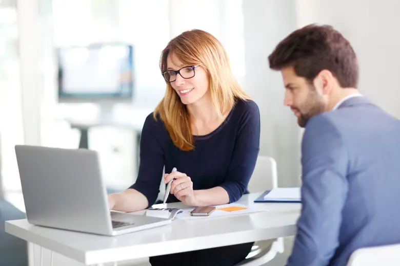 A professional working woman showing her laptop screen to a professional working man.