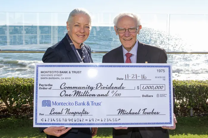 Two bank associates hold a large check with a million-dollar amount that is addressed to local nonprofits.