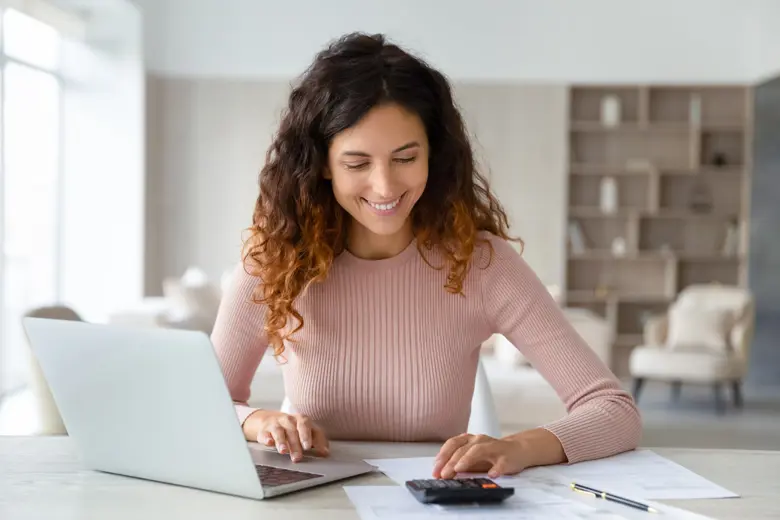 A woman using a calculator while using her laptop.