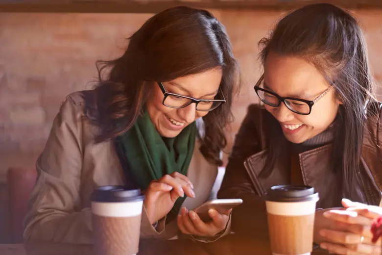 Two women at a cafe shop looking at a phone together.