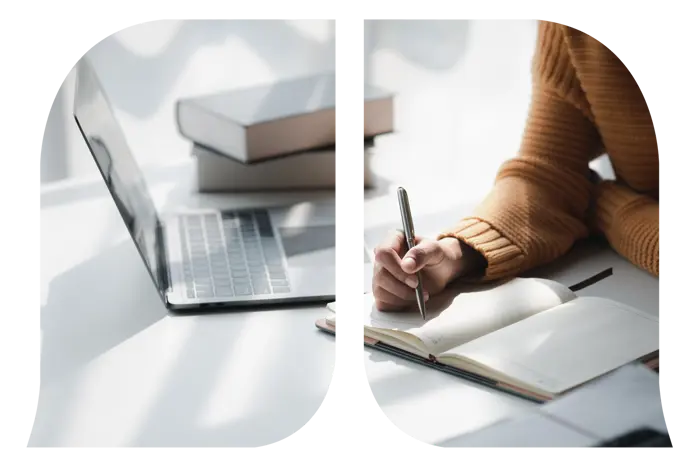 A woman's hand writing down notes on a notebook next to her laptop.