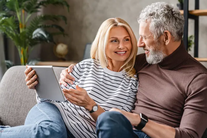 An elder couple are cuddling on a couch with an ipad in hand.